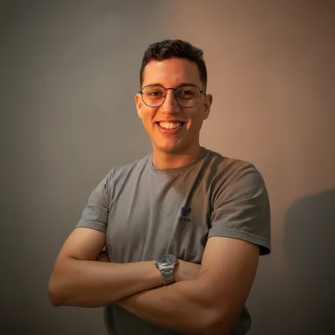 The same man as a studio headshot with arms crossed on a dark backdrop