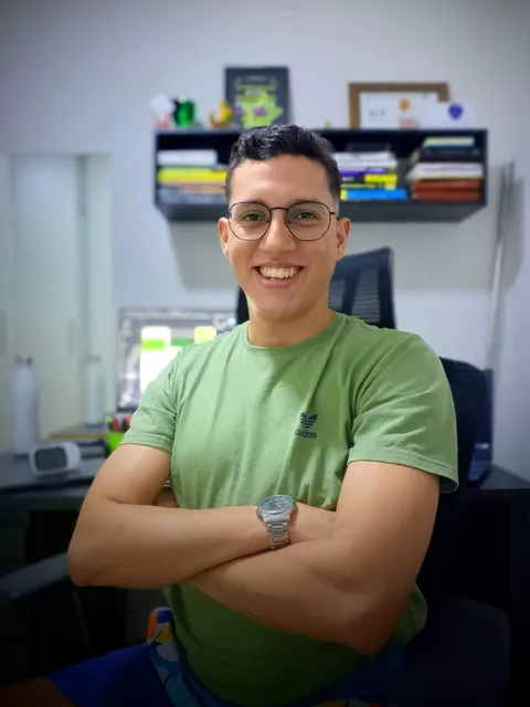 Phone selfie of a smiling man in a green t-shirt at a home office desk